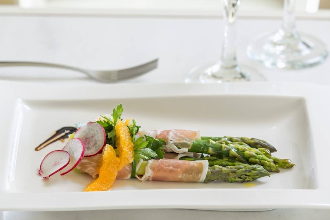 Gericht mit Spargel, Schinken und Radieschen auf einem weißen Teller im Vencia Boutique Hotel.