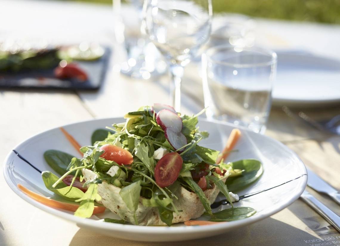 Ein frisches Salatgericht auf einem weißen Teller im Garten serviert.