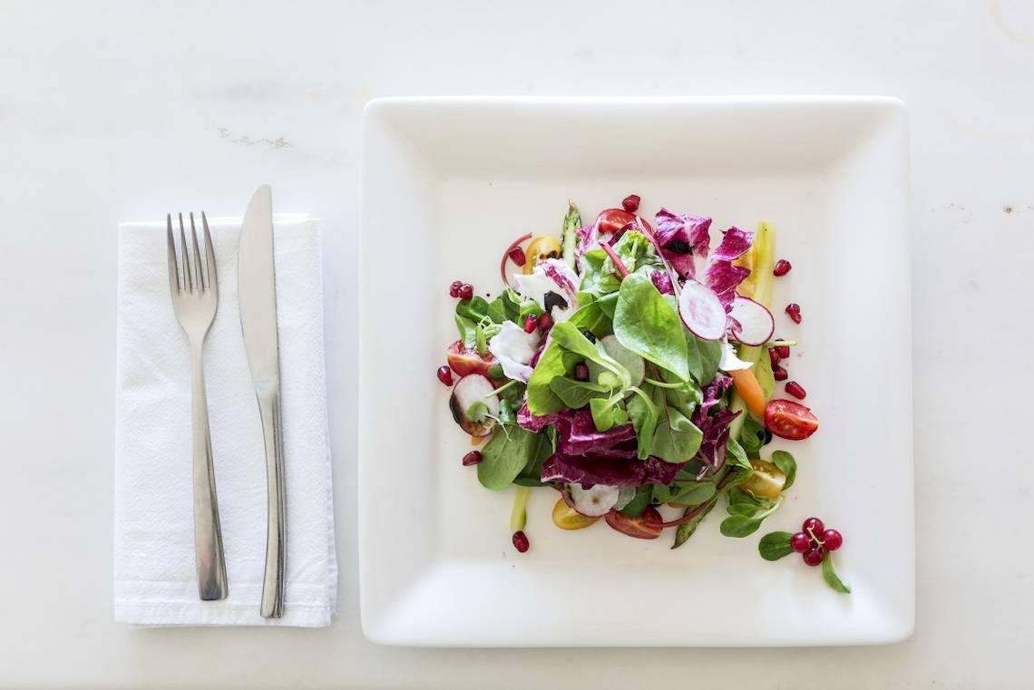 Ein Salat auf einem weißen Teller, neben einem Serviettentuch mit einem Messer und einer Gabel.