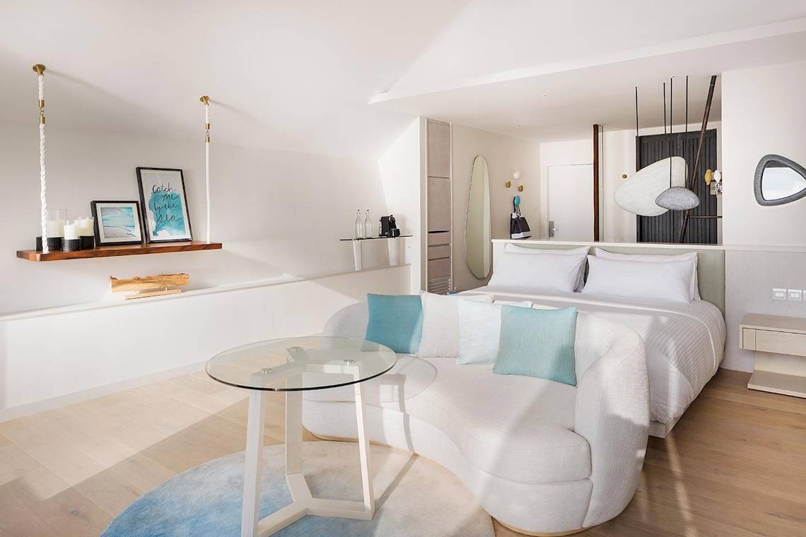 Innenansicht des Schlafzimmers im LUX South Ari Atoll Hotel mit einem großen Bett, weißen Möbeln und einem Glastisch.