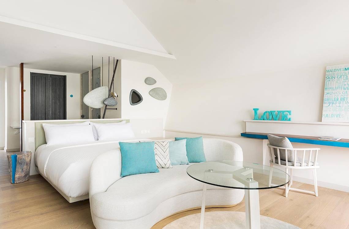 Innenansicht der Suite im LUX South Ari Atoll Hotel mit Bett, Couch, Tisch und Dekor.