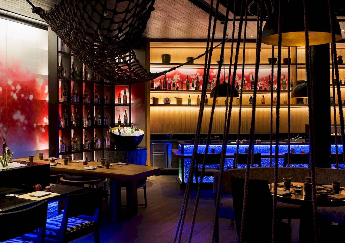 Innenansicht der Bar im LUX South Ari Atoll Hotel mit dekorierten Regalen, blau beleuchteter Theke und stimmungsvoller Beleuchtung.