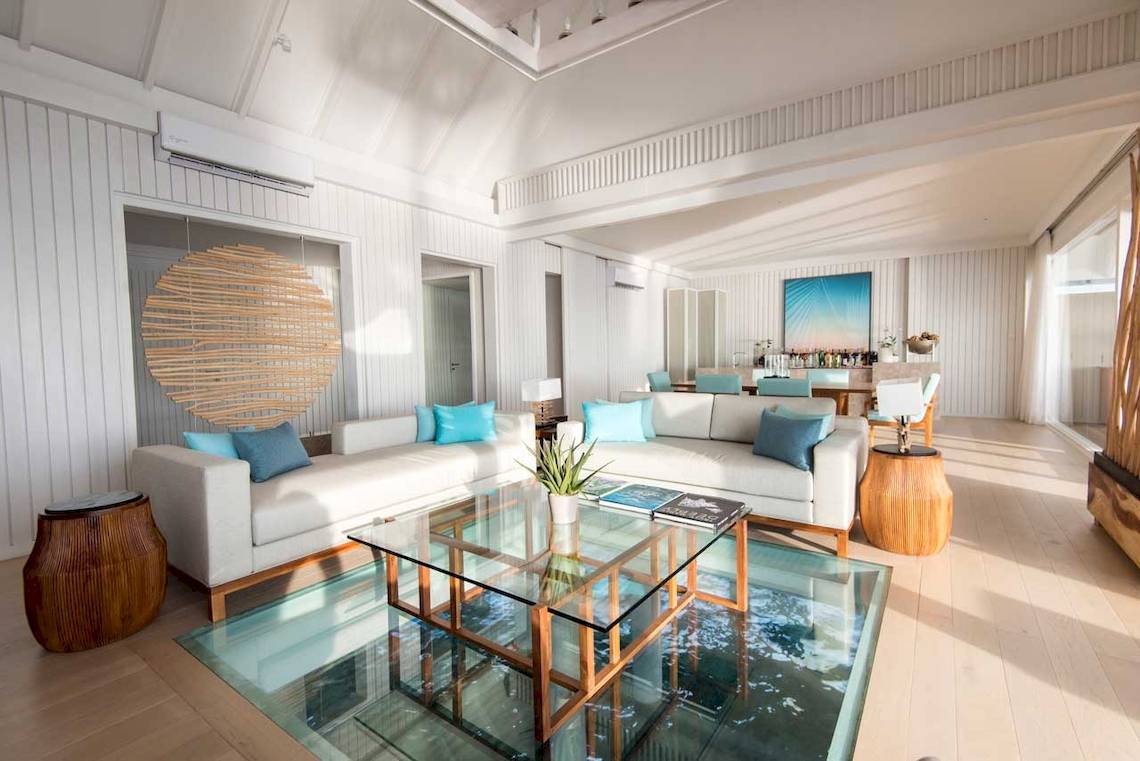 Wohnbereich des LUX South Ari Atoll Hotels mit zwei weißen Sofas, einem Glastisch und einer Glasbodenplatte.