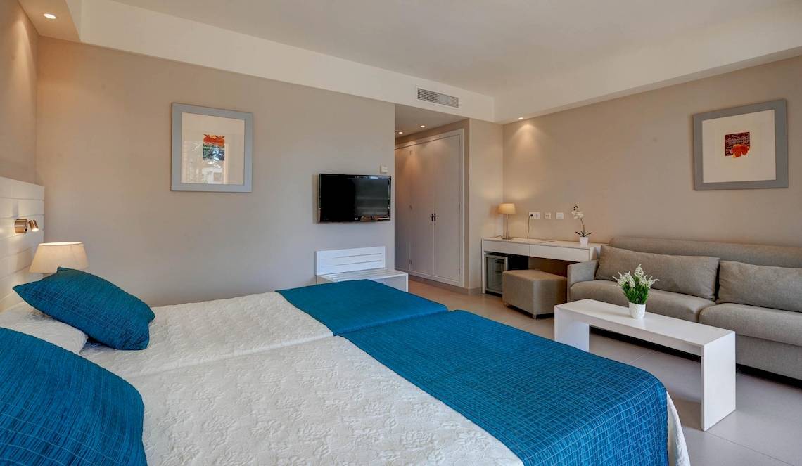 Innenansicht eines Doppelzimmers im Hipotels Said Hotel mit zwei Betten, einem Fernseher und einer Couch.