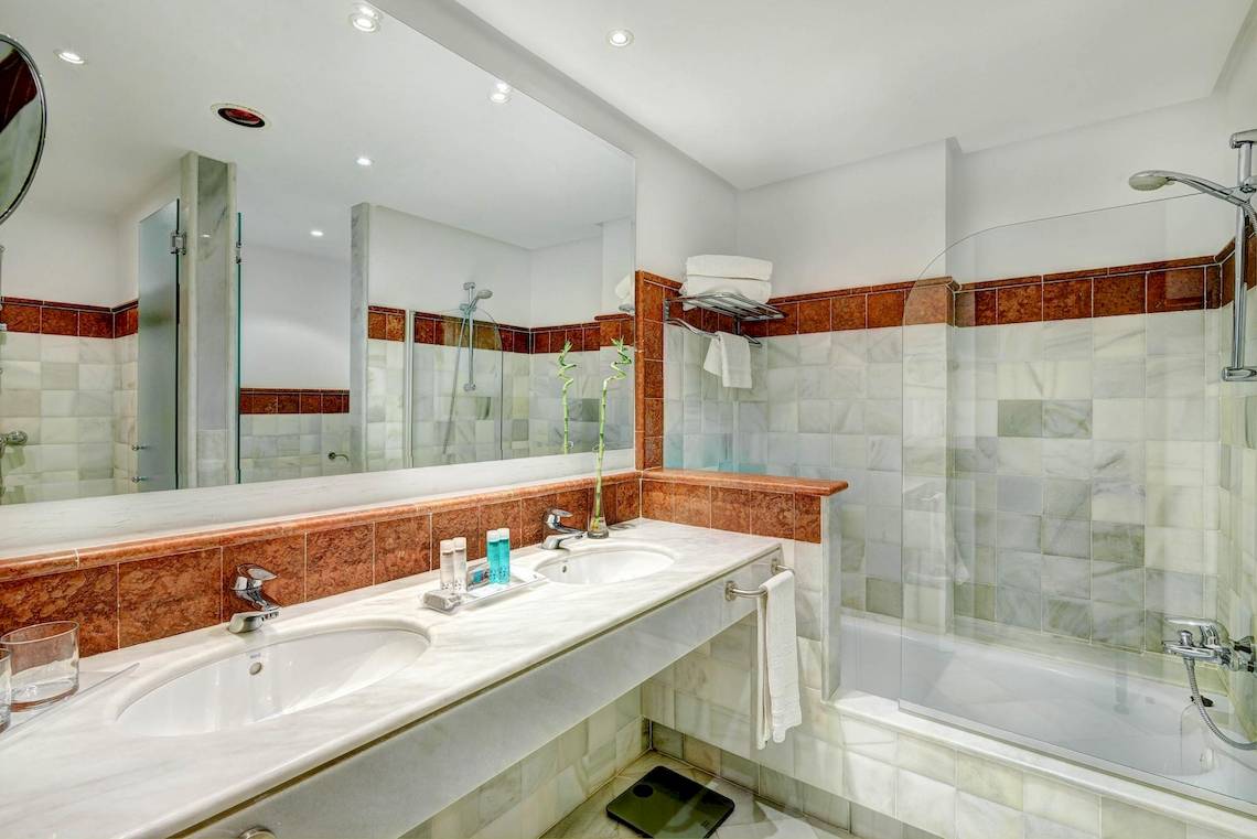 Badezimmer des Hipotels Said mit zwei Waschbecken, Badewanne und Dusche.