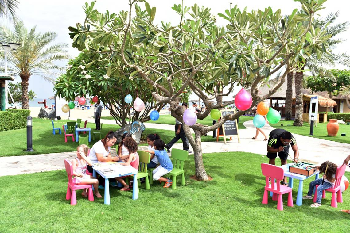 Kinder spielen im Freien unter einem Baum im Fujairah Rotana Resort & Spa.