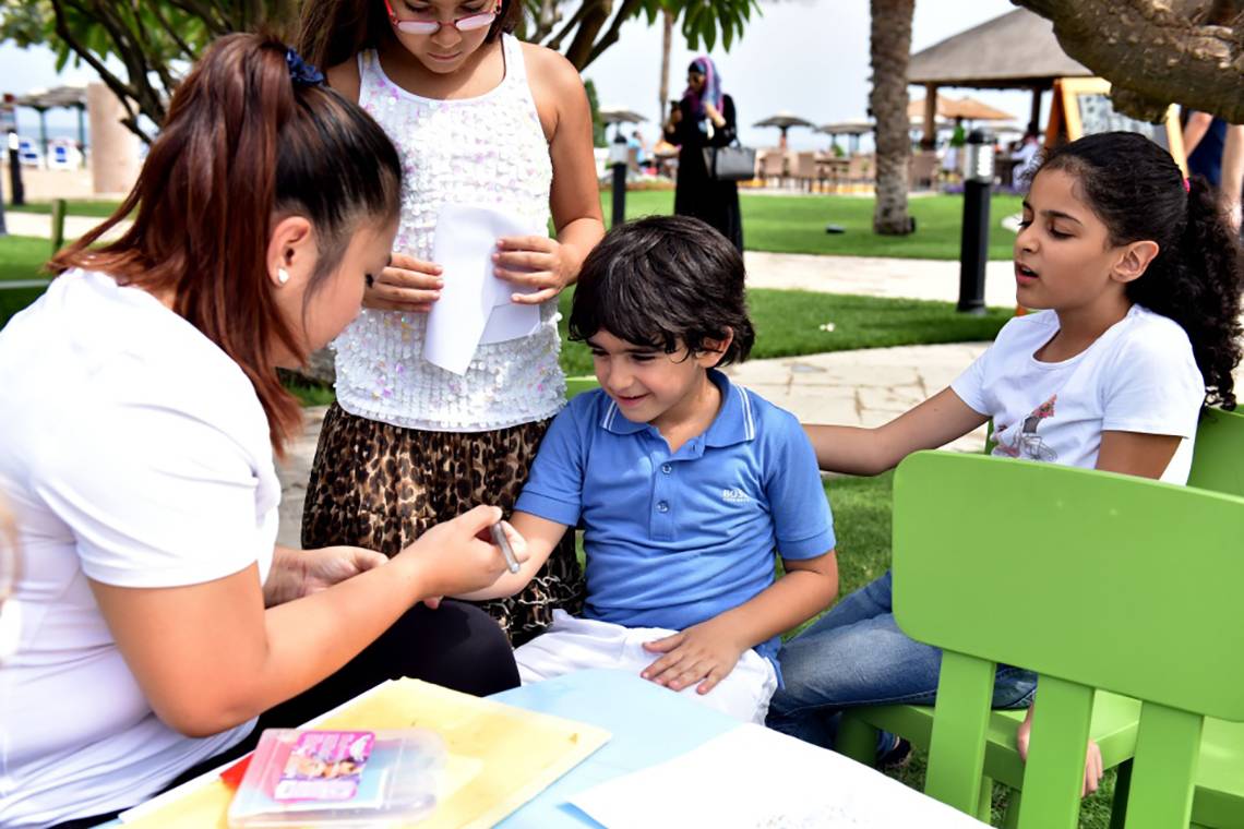 Kinder im Fujairah Rotana Resort & Spa beim Malen, während eine Frau ihr Armband malt