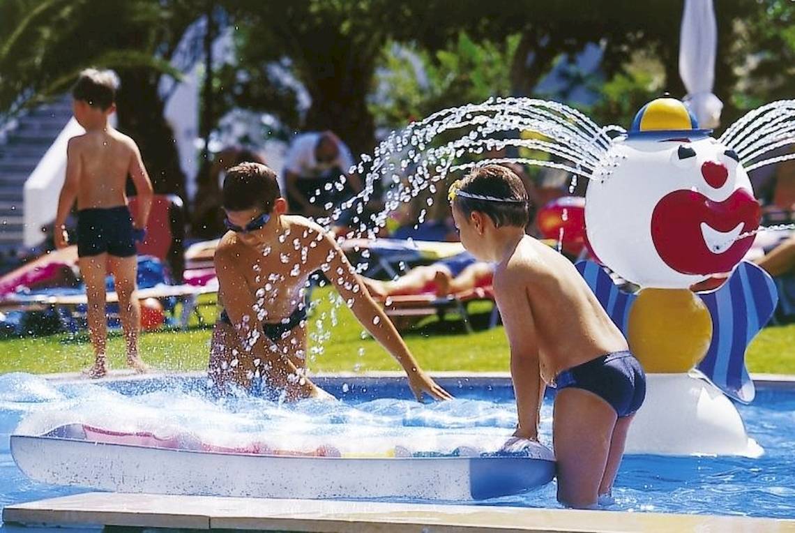 Kinder spielen im Schwimmbecken des Chrissi Amoudia Hotels mit einer Wasserfontäne.