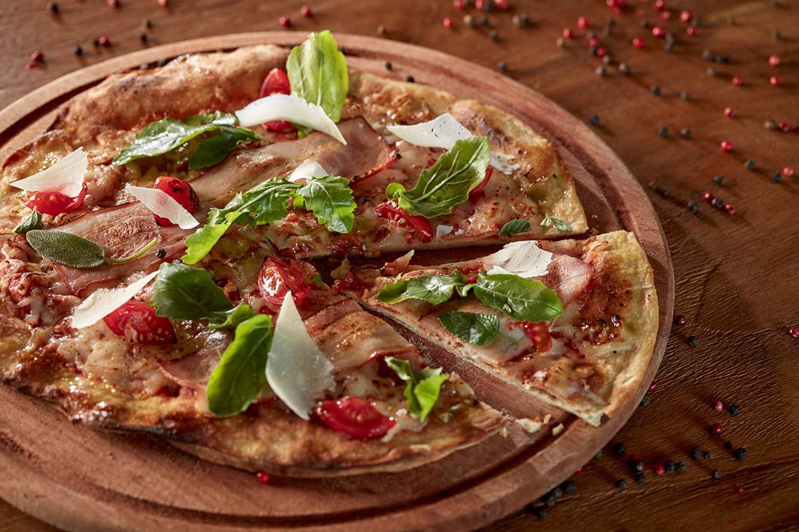 Eine Pizza mit Schinken und Basilikum auf einer Holzplatte.