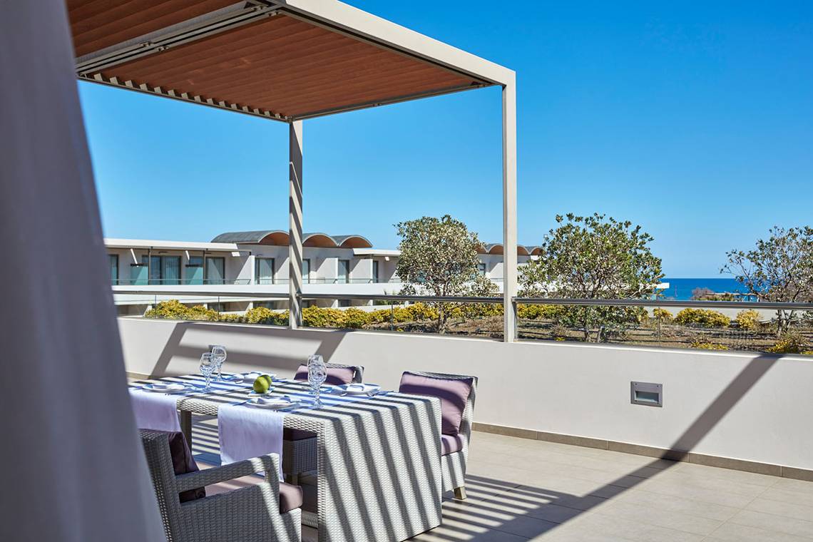 Balkon mit Meerblick im Avra Imperial Hotel mit Tisch und Stühlen unter einer Pergola.