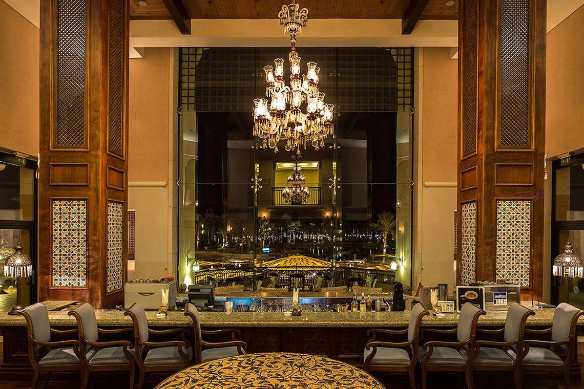 Innenansicht der Bar im Pickalbatros The Palace Port Ghalib Hotel mit großem Kronleuchter, Sitzbereich und Blick auf die Nachtlandschaft.