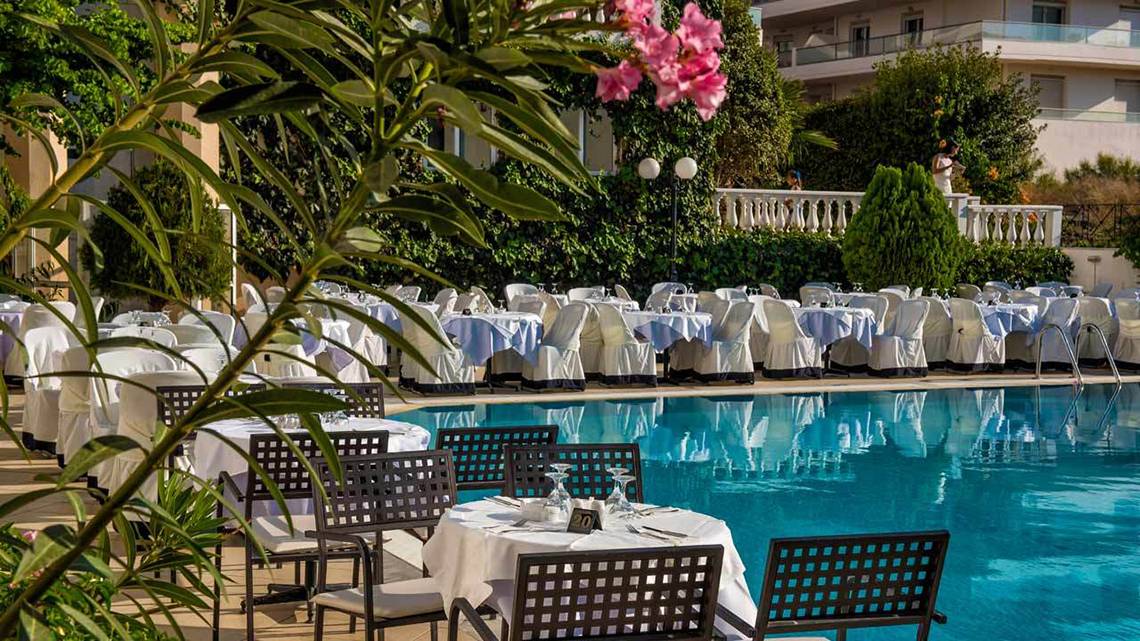 Pool-Essbereich des Hersonissos Palace Hotels mit gedeckten Tischen und Stühlen.