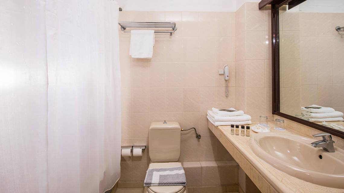 Badezimmer im Hersonissos Palace Hotel mit Dusche, Toilette, Handtüchern und Kosmetikartikeln.