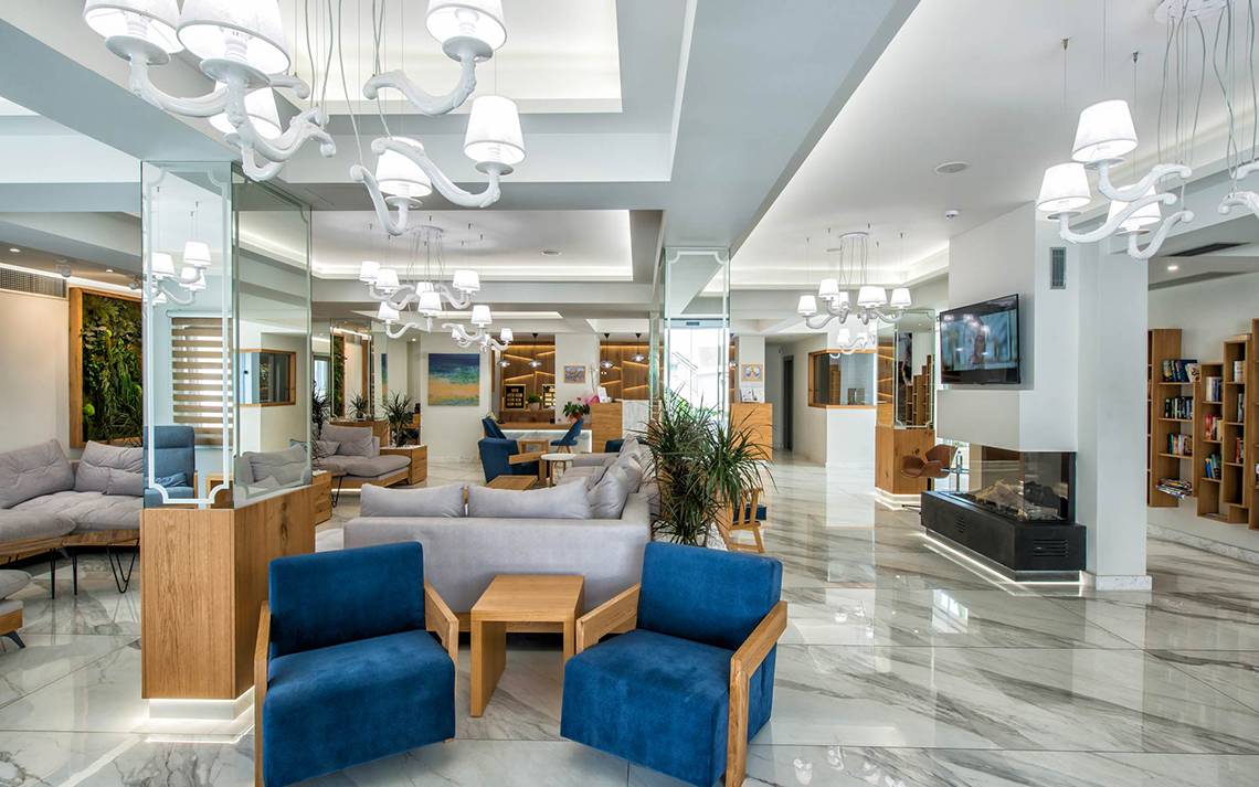 Lobby des Odyssia Beach Hotels mit modernen Möbeln, hellen Wänden und hängenden Kronleuchtern.