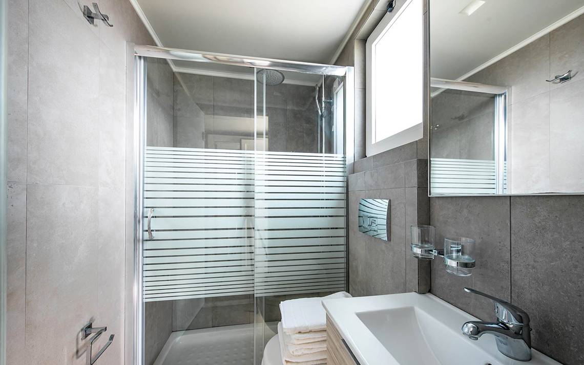 Badezimmer des Odyssia Beach Hotels mit einer Glasdusche, einem Waschbecken und einem Spiegel.