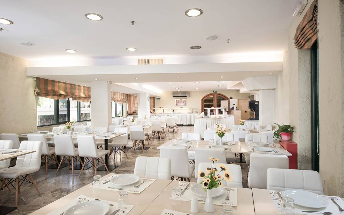 Innenbereich des Speisesaals im Odyssia Beach Hotel mit weißen Möbeln und Tischdekoration.