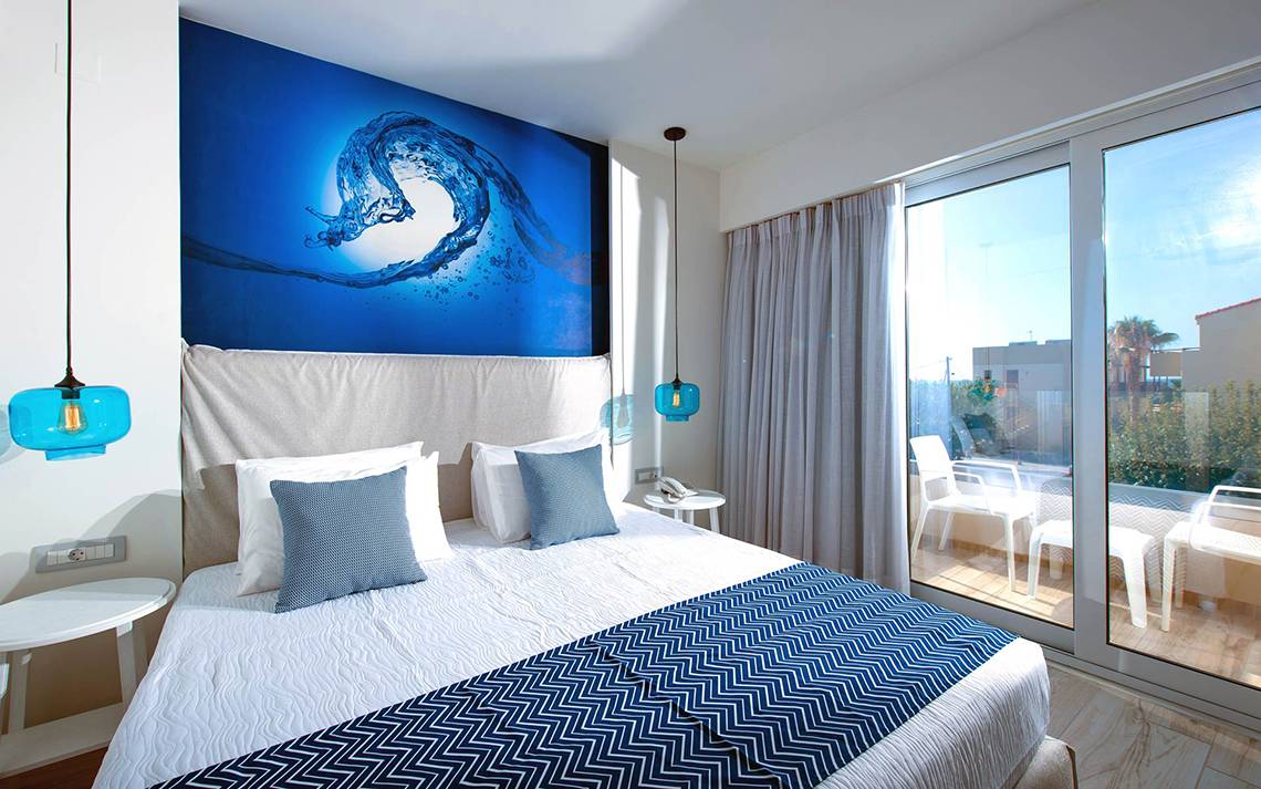 Schlafzimmer im Odyssia Beach Hotel mit blauer Wand, Doppelbett und großem Fenster.