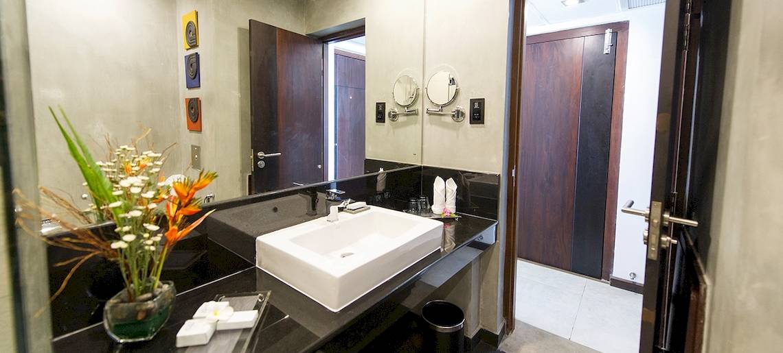 Badezimmer im Club Hotel Dolphin mit weißem Waschbecken, Spiegel und Blumenvase.