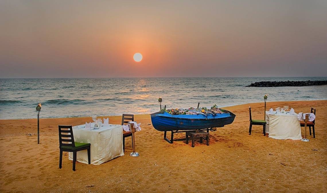 Strand mit Tisch am Abend vor dem Club Hotel Dolphin mit Blick auf den Ozean und den Sonnenuntergang.