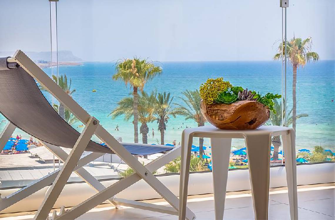 Aussicht von der Terrasse des Stamatia Hotels auf das Meer mit Palmen und einem Tisch mit einer Pflanze.