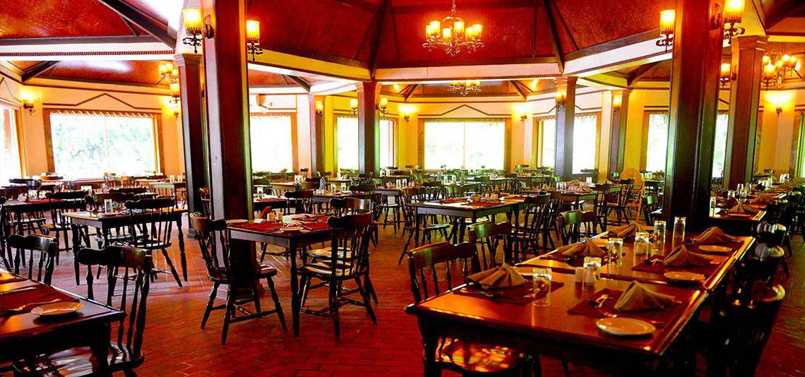 Ein Restaurant des Biyadhoo Island Resorts mit vielen Tischen und Stühlen, Deckenlampen und großen Fenstern.
