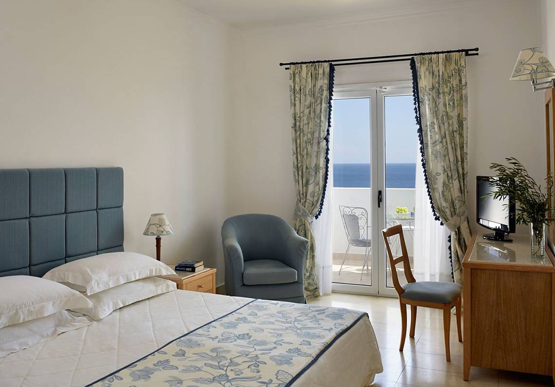 Schlafzimmer im Mitsis Norida Beach Hotel mit Meerblick, Bett, Sessel und Schreibtisch.
