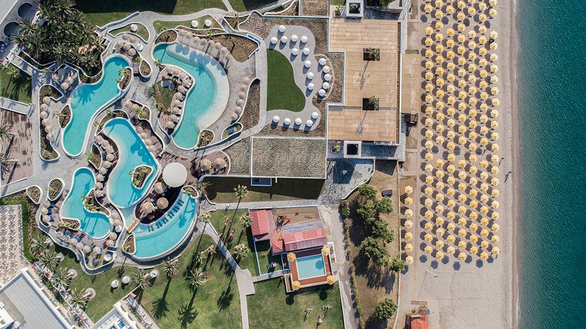 Luftaufnahme des Mitsis Norida Beach Hotels mit Swimmingpools, Sonnenschirmen und Strand