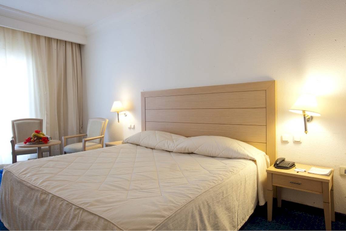 Doppelbettzimmer im El Mouradi Mahdia Hotel mit weißem Bett, zwei Sesseln, Nachttisch und Lampen