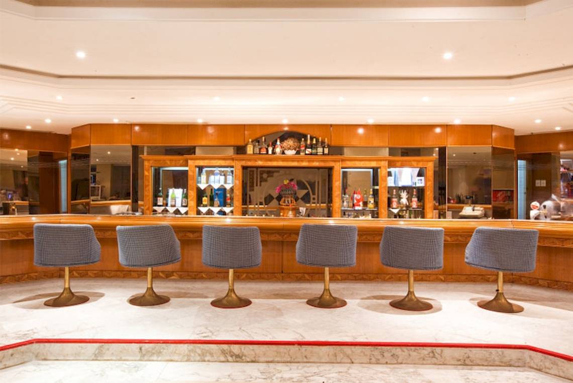 Innenansicht der Bar im El Mouradi Mahdia Hotel mit sechs grauen Stühlen und einer Theke.