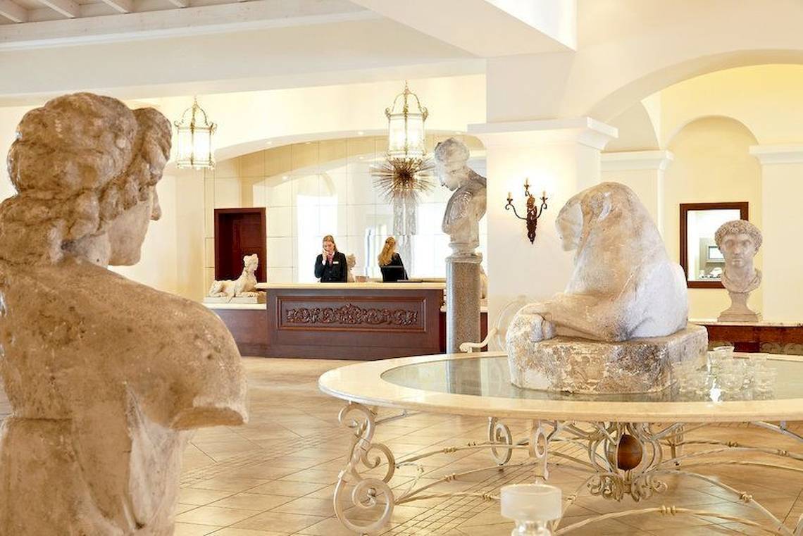 Ein Hotellobby mit Statuen, einer Rezeption und einer Glastisch in der Mitte.