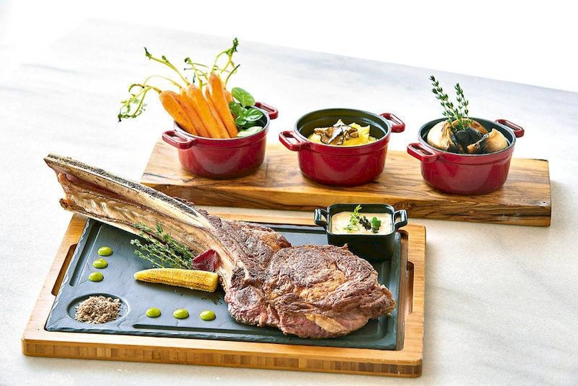 Ein Steak und Gemüse auf einer Holzunterlage mit Beilagen in Töpfen.