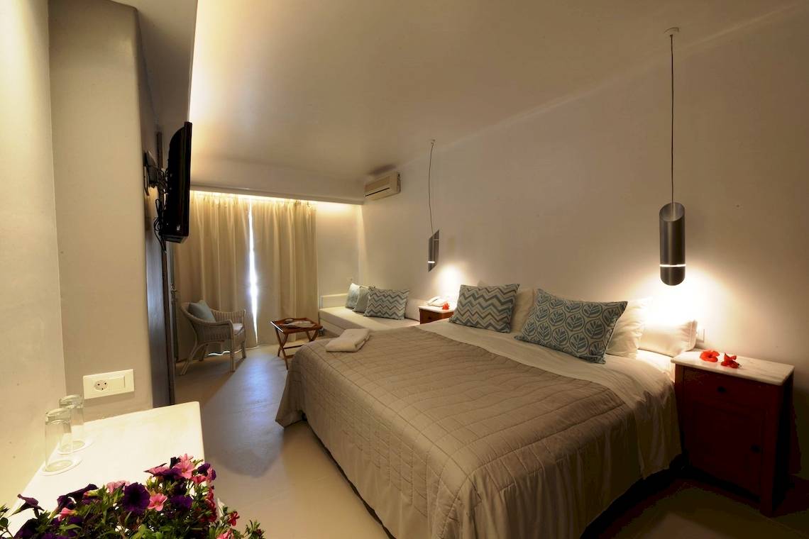 Schlafzimmer im MykonosView Hotel mit einem großen Bett, zwei Nachttischen, einem Fernseher und einem Fenster mit Vorhängen.