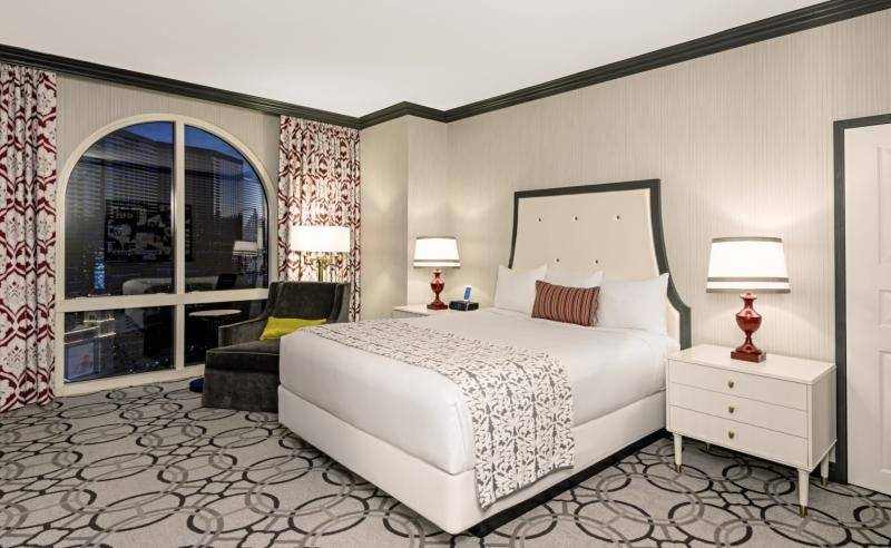 Hotelzimmer im Paris Las Vegas mit großem Bett, zwei Nachttischen und einem Sessel