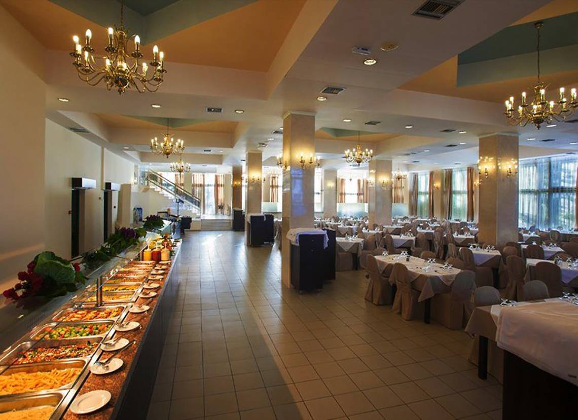 Innenansicht des Restaurants im Smy Kos Beach & Splash Hotel mit vielen Tischen und Stühlen, Buffet und Kronleuchtern.