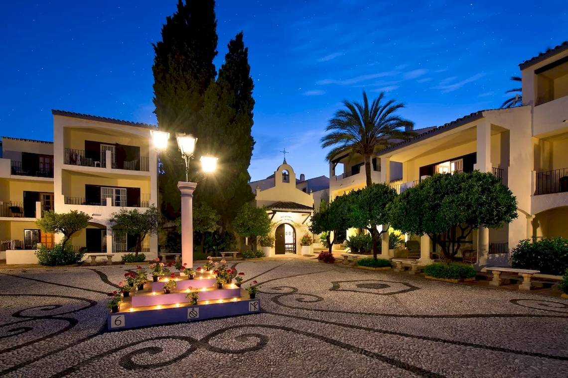 Der Eingang des Bluebay Banus Hotels bei Nacht, mit beleuchteten Blumen und Laternen.
