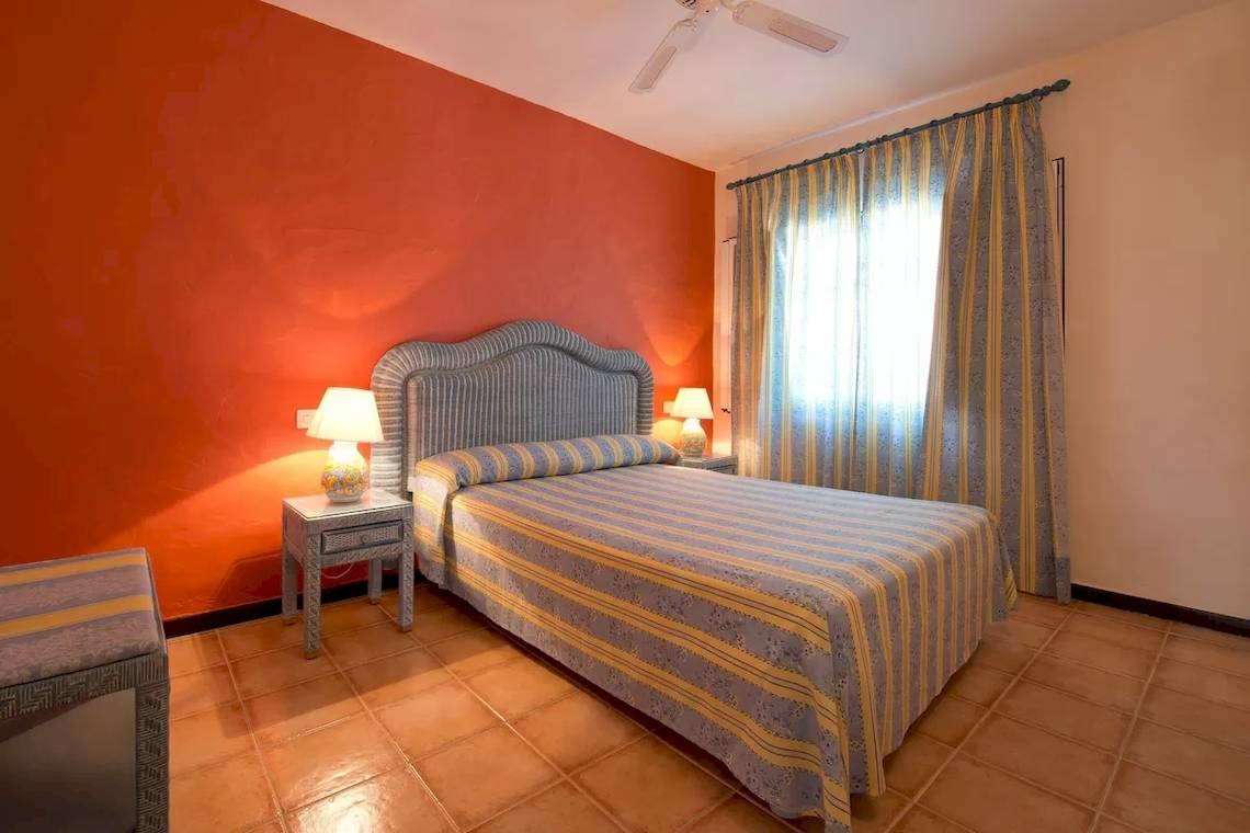 Doppelbettzimmer im Bluebay Banus Hotel mit oranger Wand, gelber Bettwäsche und zwei Nachttischen mit Lampen.