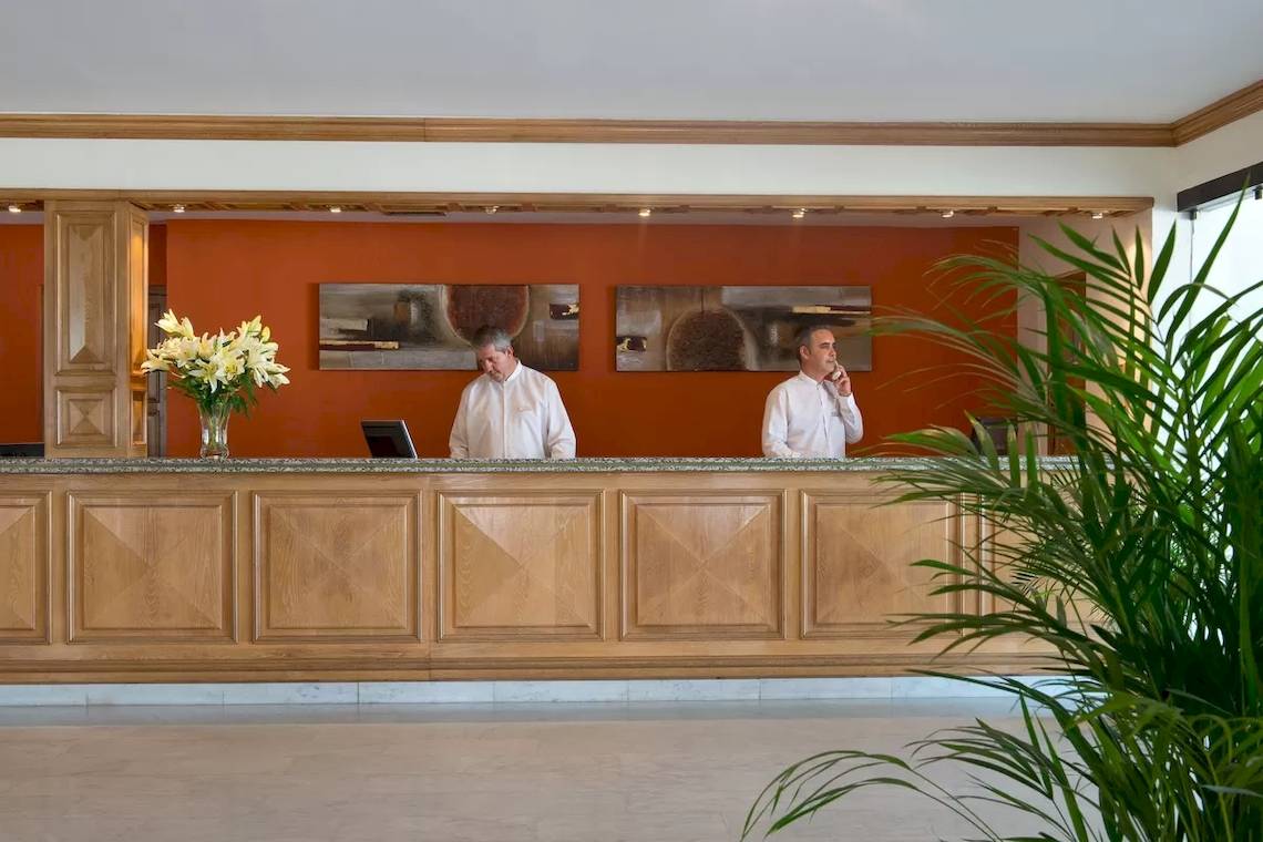 Empfangsbereich des Bluebay Banus Hotels mit zwei Mitarbeitern und einem Blumenstrauß