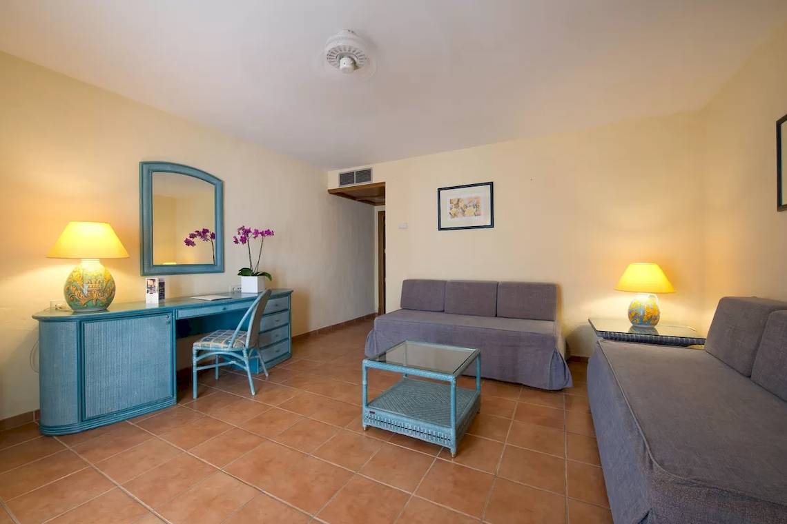 Wohnzimmer im Bluebay Banus Hotel mit Schreibtisch, Stühlen, Sofas und Lampen.