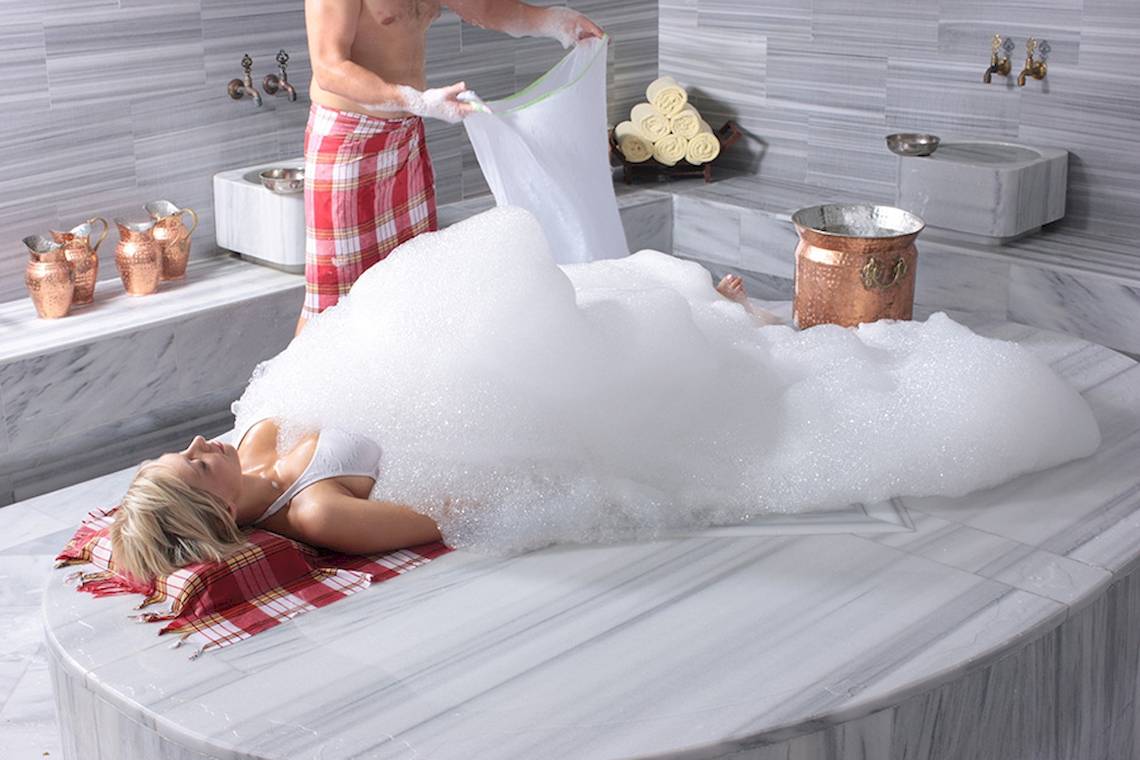 Eine Frau liegt in einem Schaumbad im Rixos Premium Dubrovnik, während ein Mann neben ihr steht.