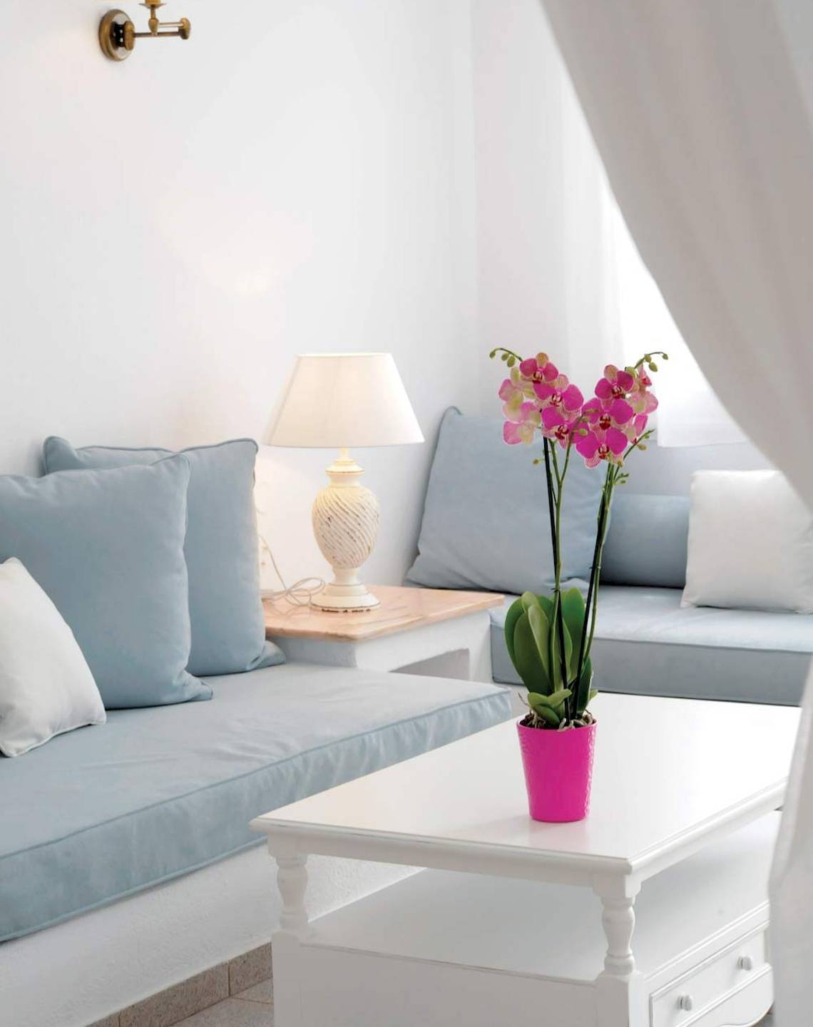 Wohnzimmer des Kamari Hotels mit weißem Sofa, Kissen, Tisch, Lampe und Orchidee