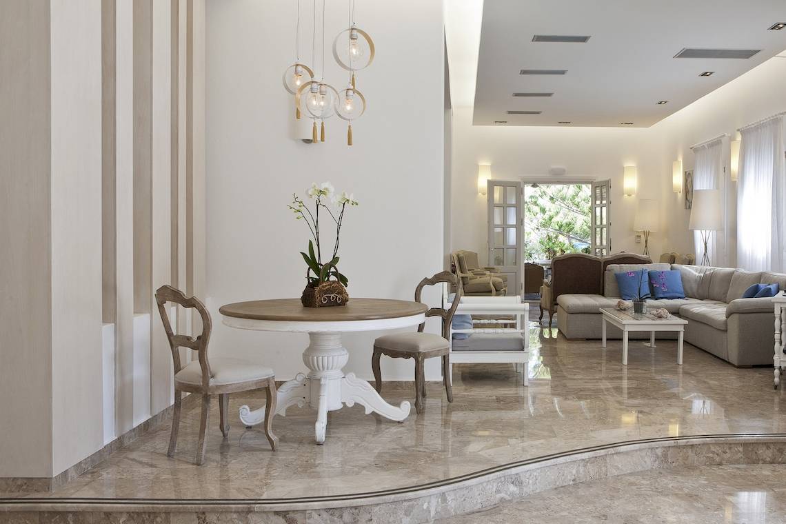 Wohnzimmer des Kamari Hotels mit weißem Tisch, Stühlen, Couch und hellem Interieur