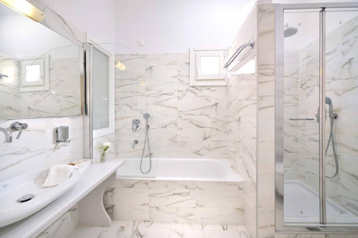 Ein elegantes Badezimmer im Kamari Hotel mit Marmorwänden, einer Badewanne und einer separaten Dusche.