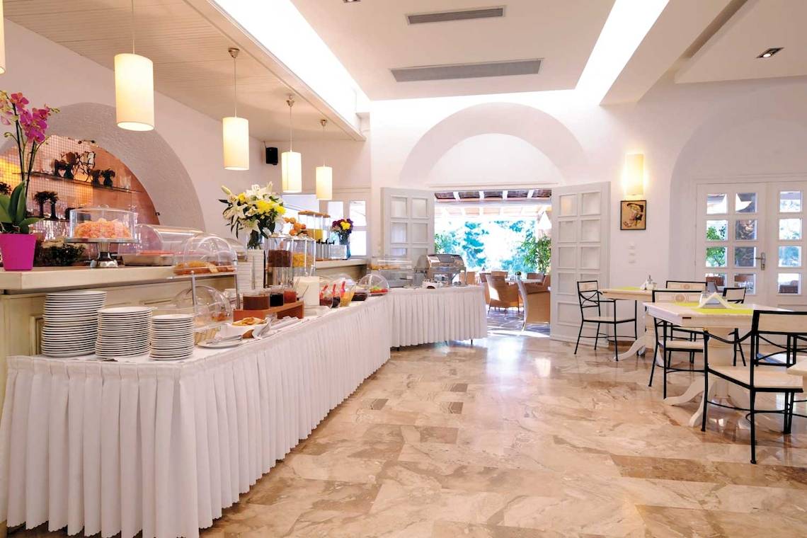 Frühstücksbuffet im Kamari Hotel mit vielen Speisen und Tisch mit Stühlen.