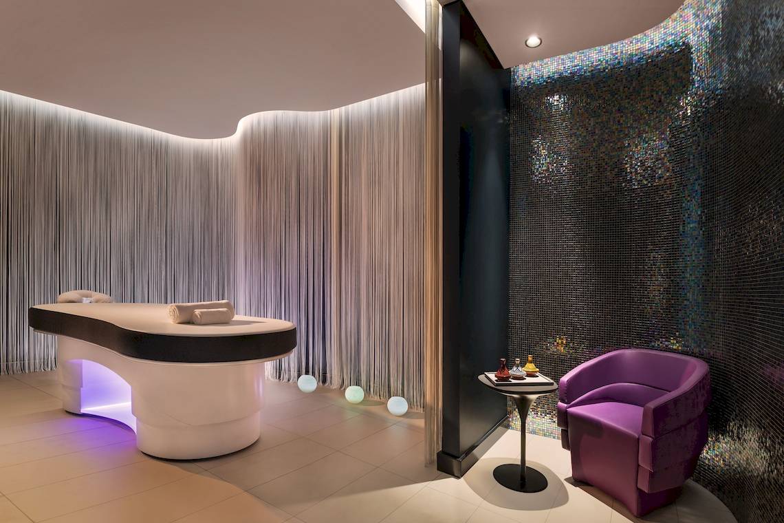 Behandlungsraum im W Dubai - The Palm Hotel mit Massageliege und violettem Stuhl.