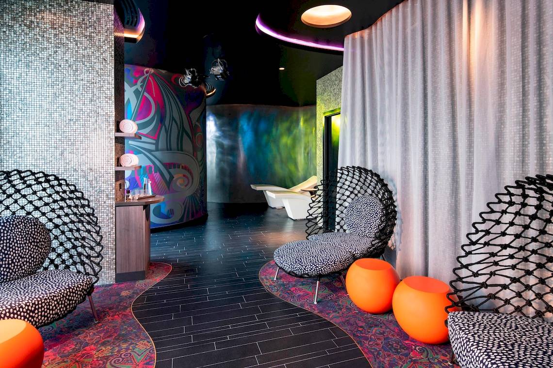 Loungebereich im W Dubai - The Palm mit bunten Wandmalereien, modernen Möbeln und orangefarbenen Hockern.