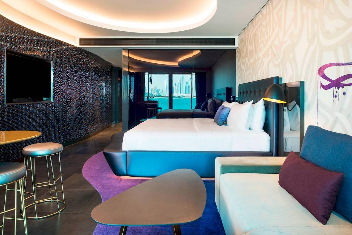 Innenansicht der Suite im W Dubai - The Palm mit Bett, Sofa, Tisch und Aussicht auf die Stadt.