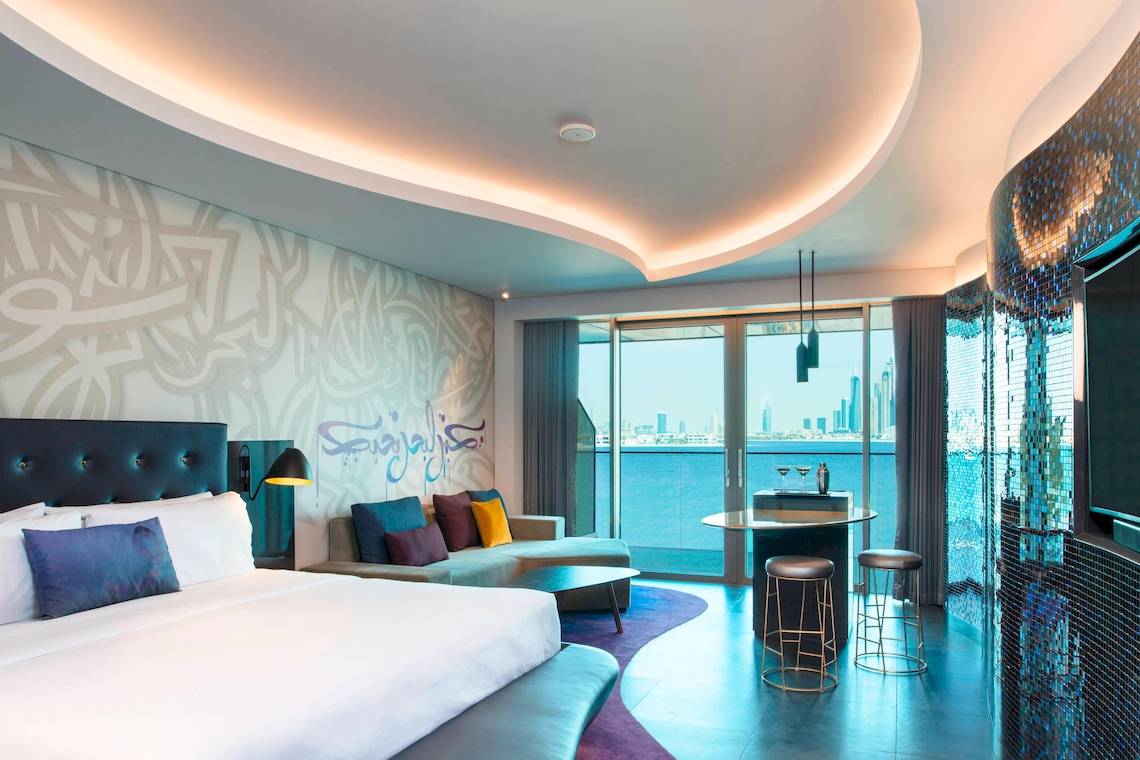 Innenansicht der Suite im W Dubai - The Palm mit Bett, Sofa, Tisch und Meerblick.