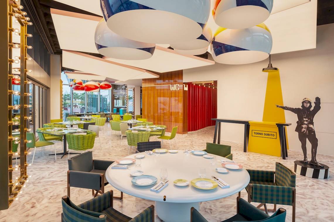 Innenbereich des W Dubai - The Palm Hotels mit runden Tischen, bunten Stühlen und Kunstwerken.