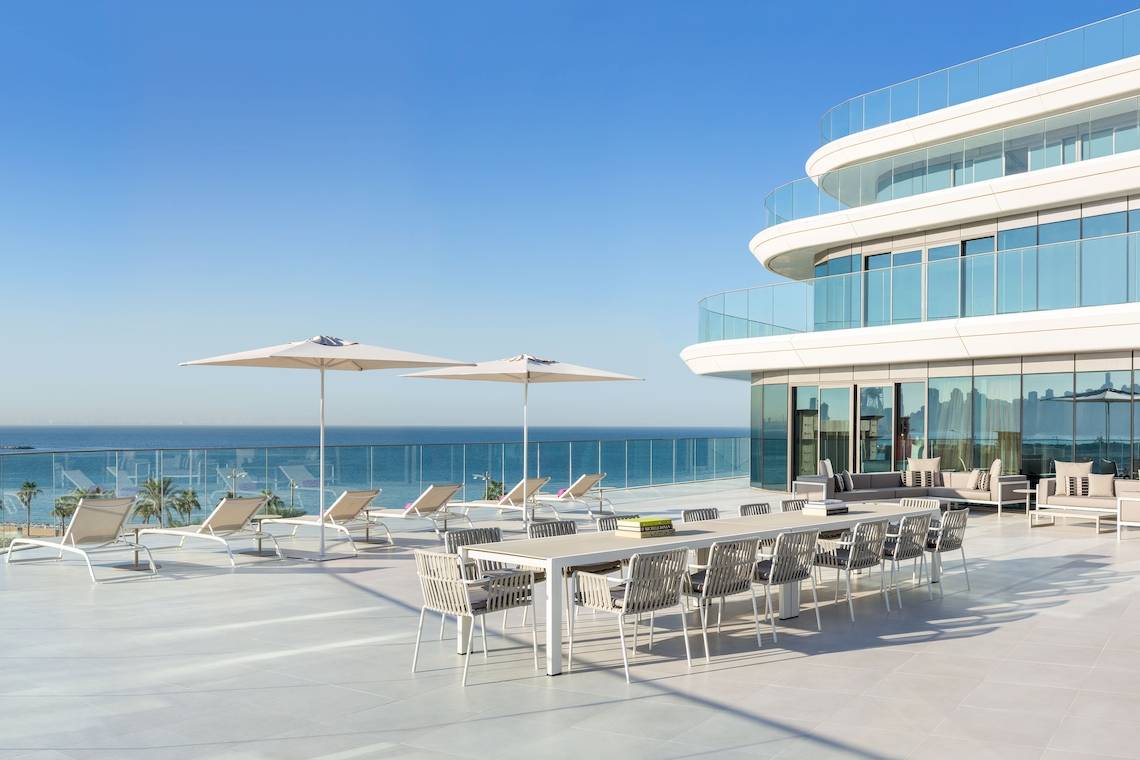 Außenterrasse des W Dubai - The Palm mit Blick auf das Meer, Lounge-Sesseln und Sonnenschirmen.