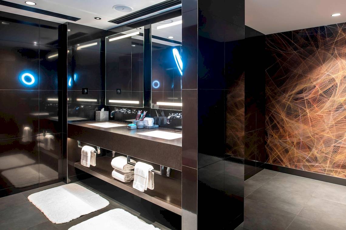 Modernes Badezimmer im W Dubai - The Palm Hotel mit schwarzen Wänden, Doppelwaschbecken, Handtüchern und blauen Lichtern.